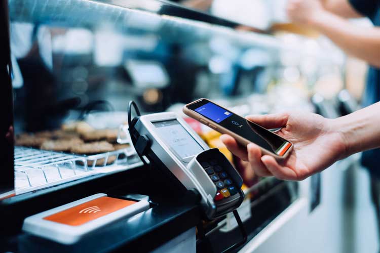 Närbild av en kvinnas hand som betalar med sin smartphone på ett kafé, skanna och betala en räkning på en kortmaskin som gör en snabb och enkel kontaktlös betalning. NFC-teknik, tap and go-koncept