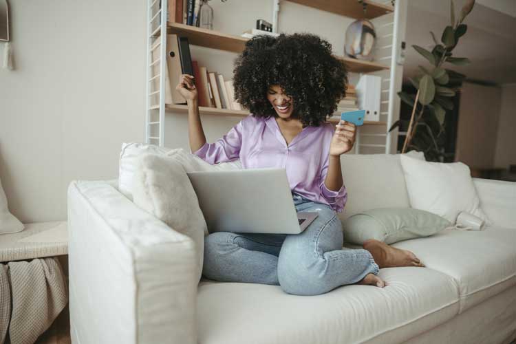 Glad kvinna med kreditkort gör online shopping på bärbar dator hemma