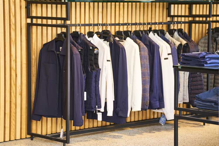 Hög med kläder som hänger från krokar i ett offentligt lager eller butik utan folk, från sidan